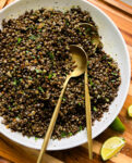 spicy black lentils in a white bowl next to lime wedges