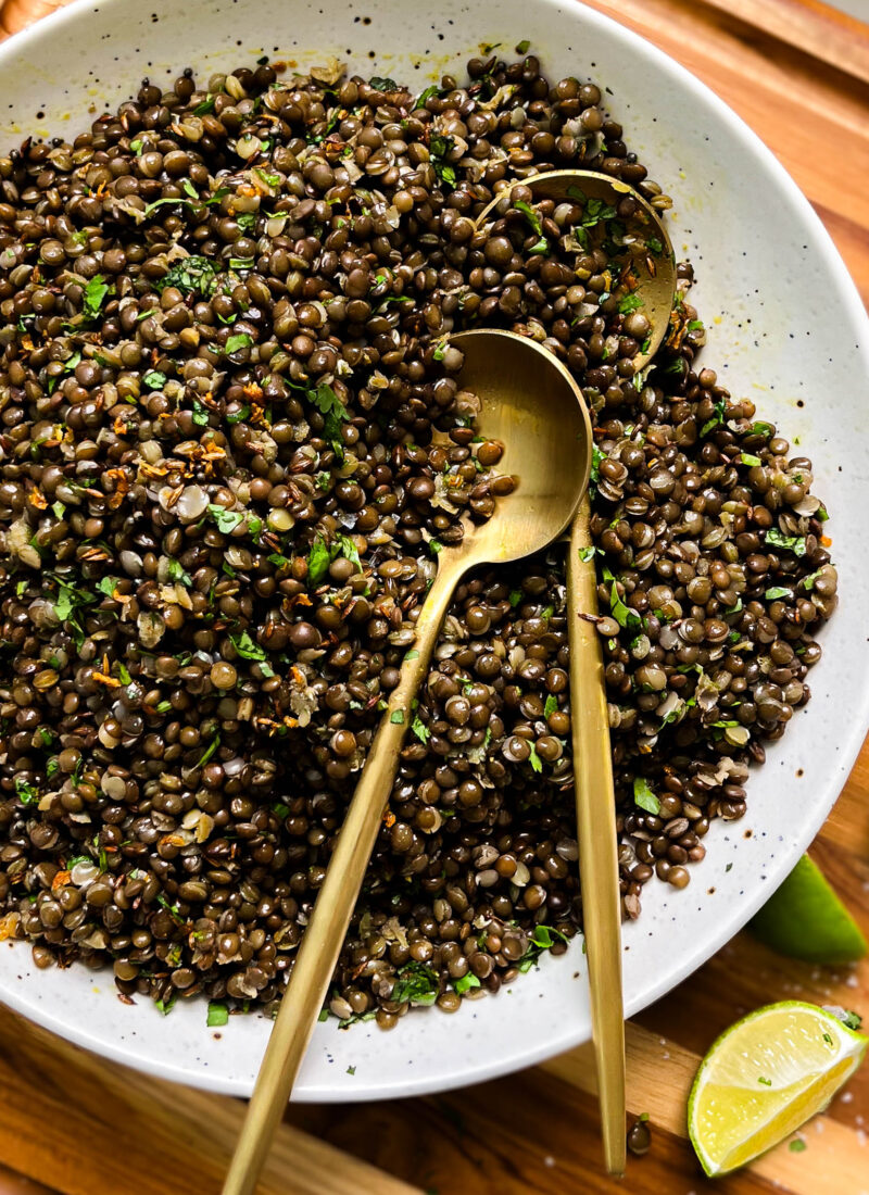 spicy black lentils in a white bowl next to lime wedges
