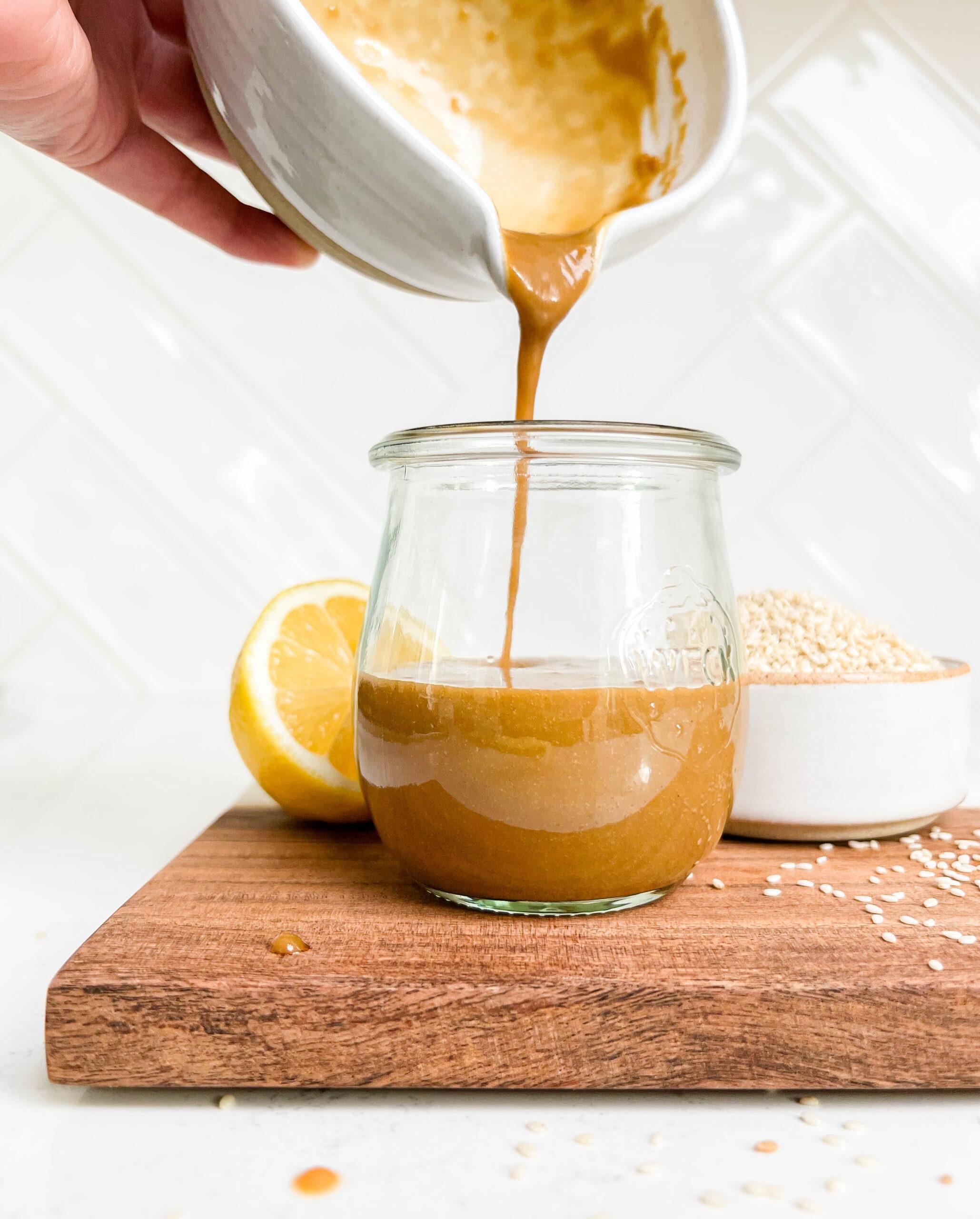 peanut dressing in a glass jar on a cutting board next to lemons and a bowl of sesame seeds