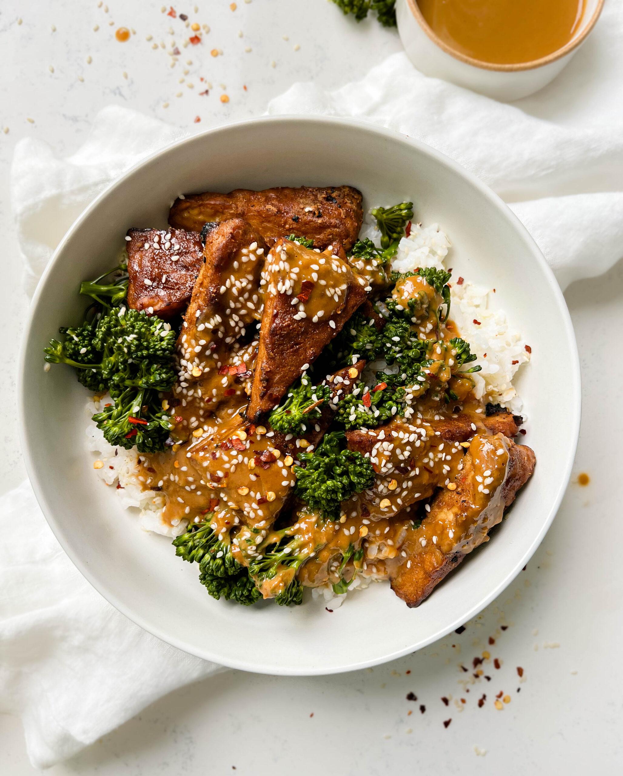 marinated peanut tempeh with white rice and broccoli next to a white linen cloth
