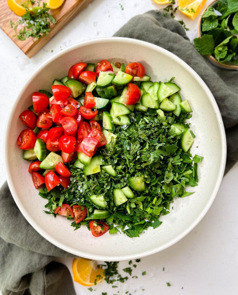 tabbouleh salad ingredients in a white bowl next to a cutting board and mint leaves