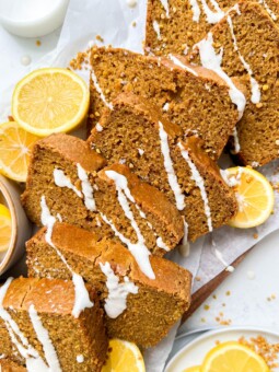 vegan lemon loaf on a cutting board with cream cheese icing drizzled on top, next to sliced lemons and a glass of milk