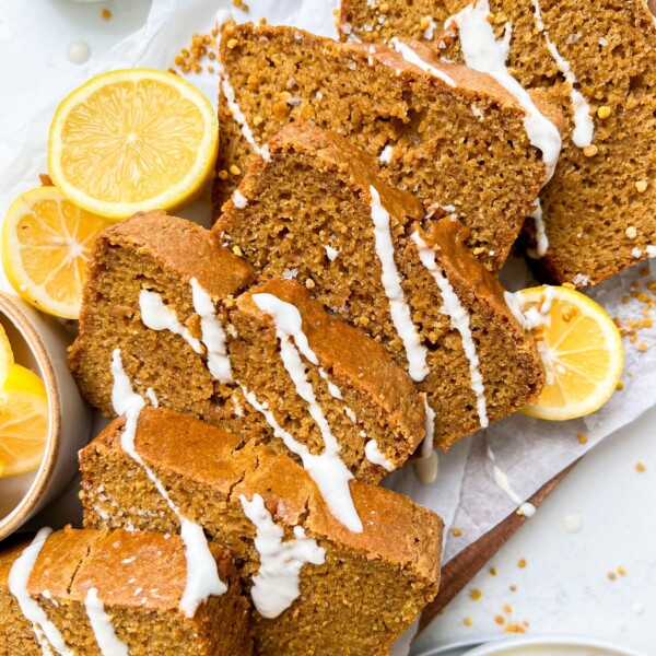 vegan lemon loaf on a cutting board with cream cheese icing drizzled on top, next to sliced lemons and a glass of milk