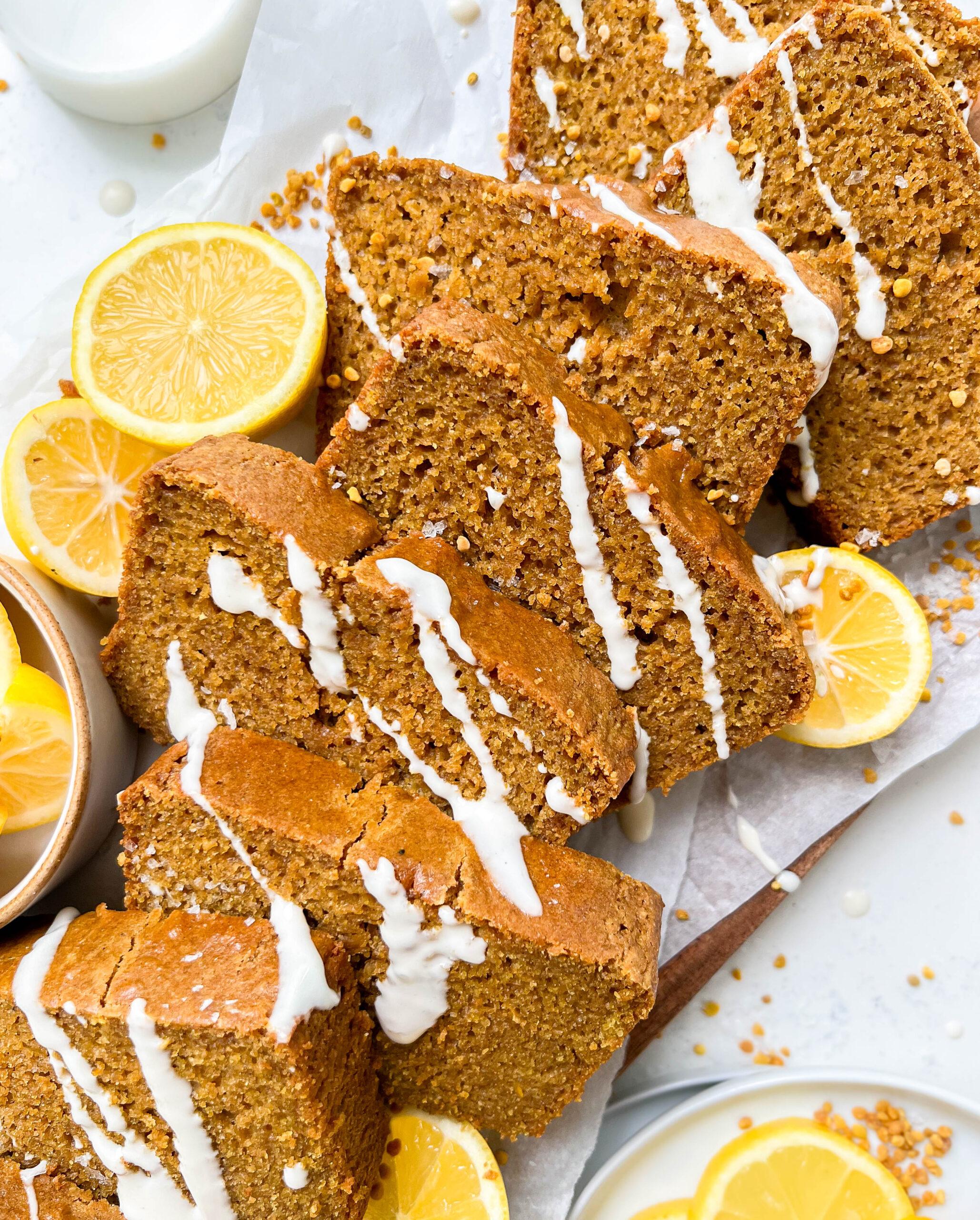 vegan lemon loaf on a cutting board with cream cheese icing drizzled on top, next to sliced lemons and a glass of milk