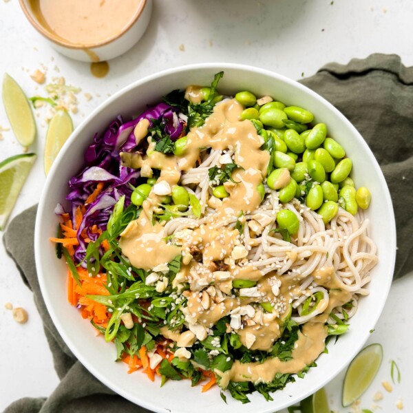 sesame peanut soba noodle salad in a white bowl next to peanut sauce