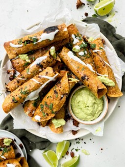 crispy baked vegan taquitos next to avocado crema sauce