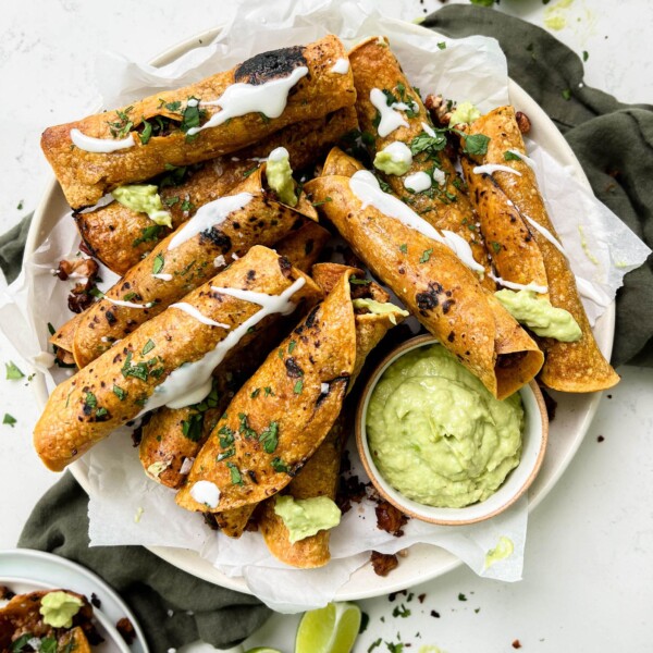 crispy baked vegan taquitos next to avocado crema sauce