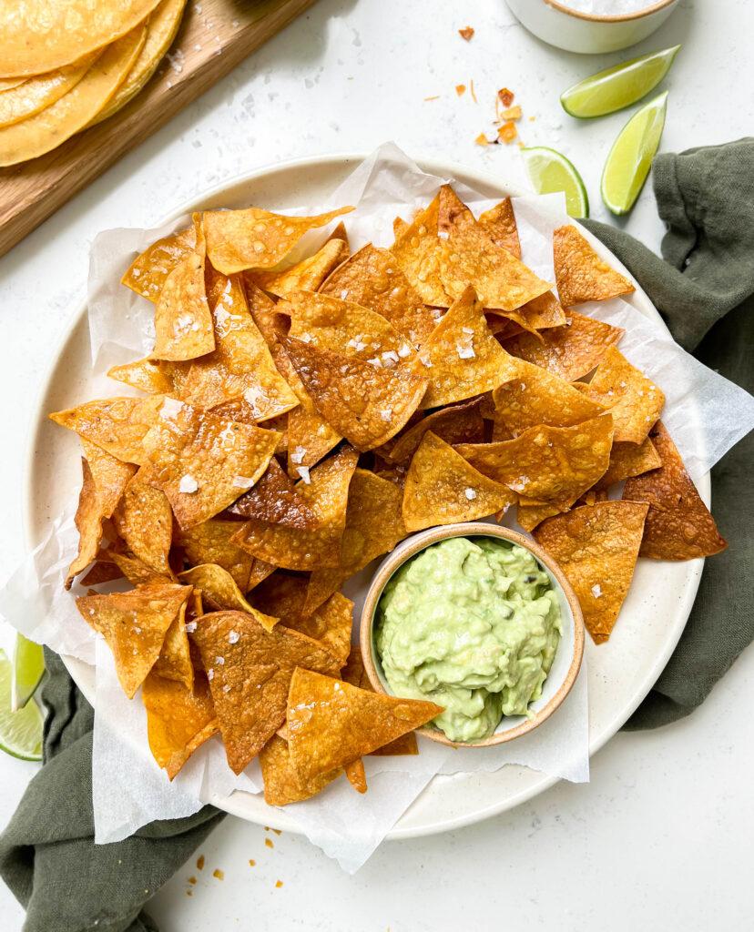 crispy homemade baked tortilla chips on a plate next to a board of tortillas, limes and avocado crema