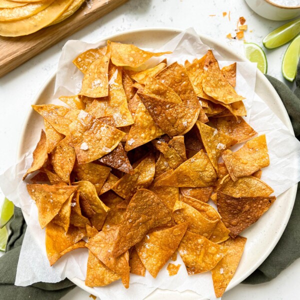 crispy homemade baked tortilla chips on a plate next to a board of tortillas and limes