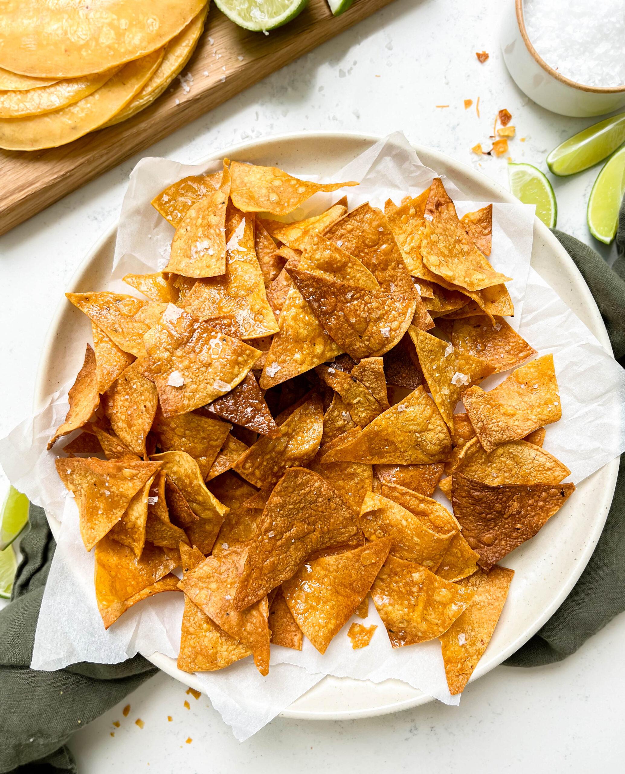 crispy homemade baked tortilla chips on a plate next to a board of tortillas and limes