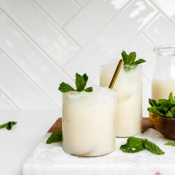 two glasses of coconut lemonade on a marble and wood cutting board