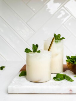 two glasses of coconut lemonade on a marble and wood cutting board