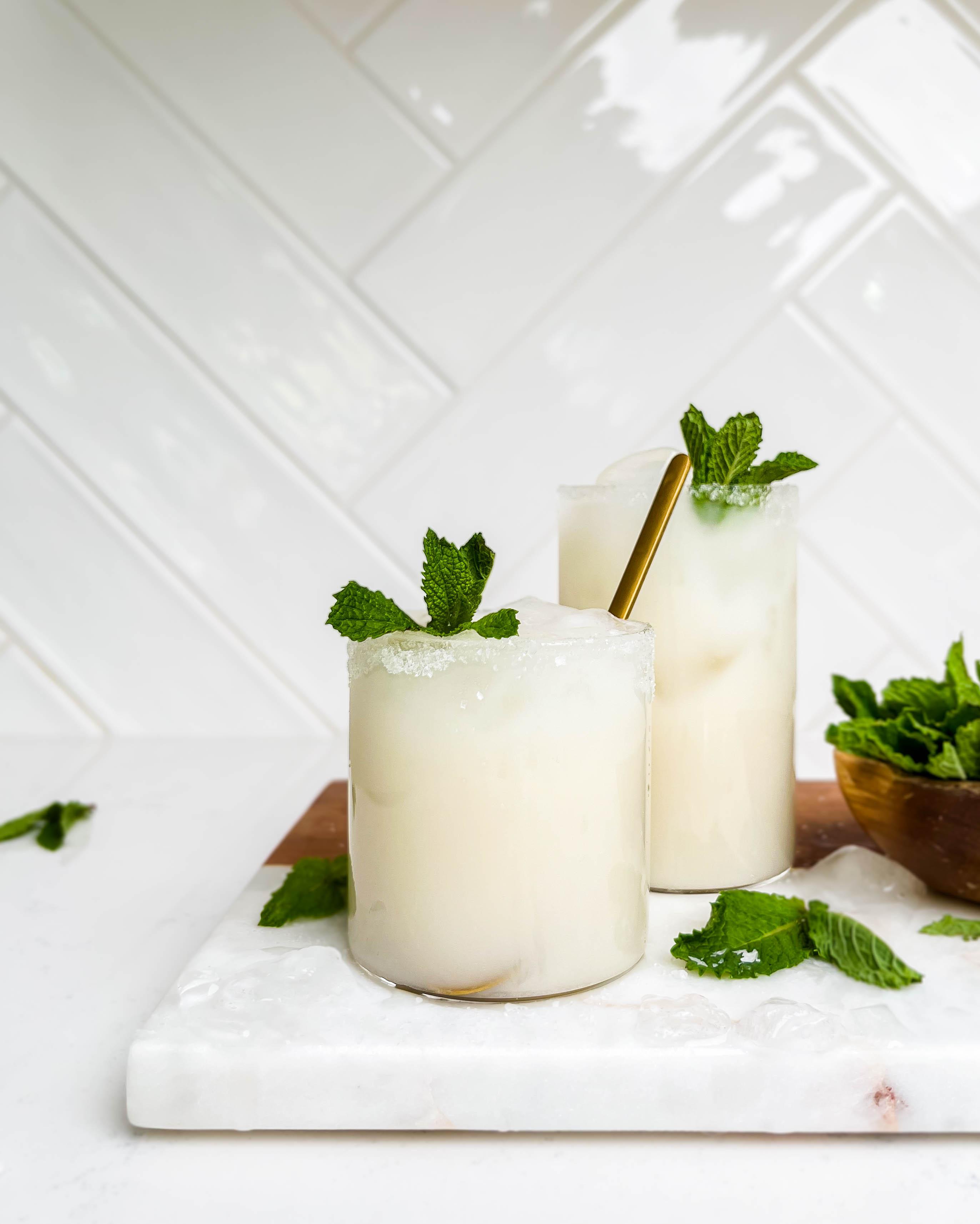 two glasses of coconut lemonade on a marble and wood cutting board