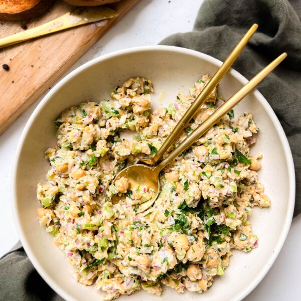 bowl of chickpea tuna salad next to a cutting board with bread and a gold knife
