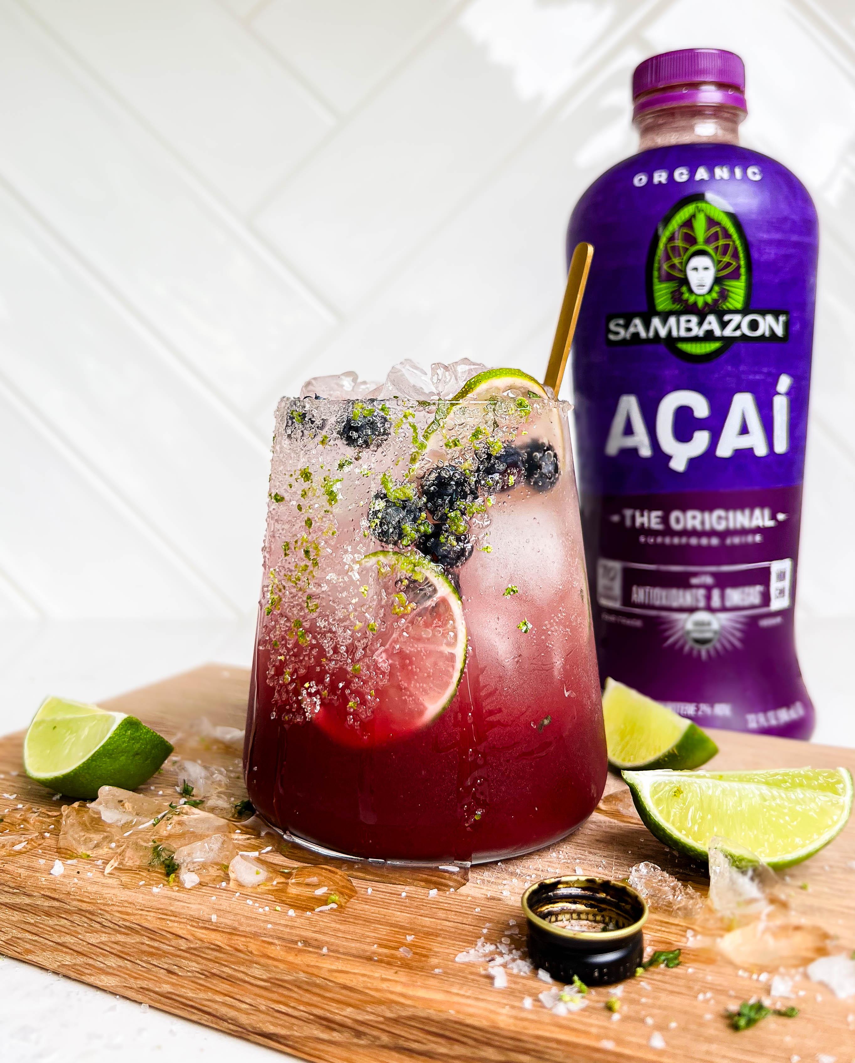 summer berry smash mocktail on cutting board with lime wedges next to a bottle of SAMBAZON acai juice