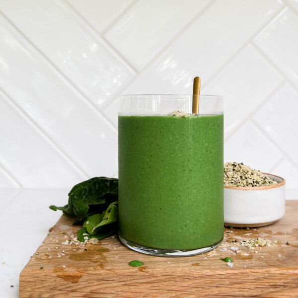 green smoothie on a cutting board next to hemp seeds and spinach leaves