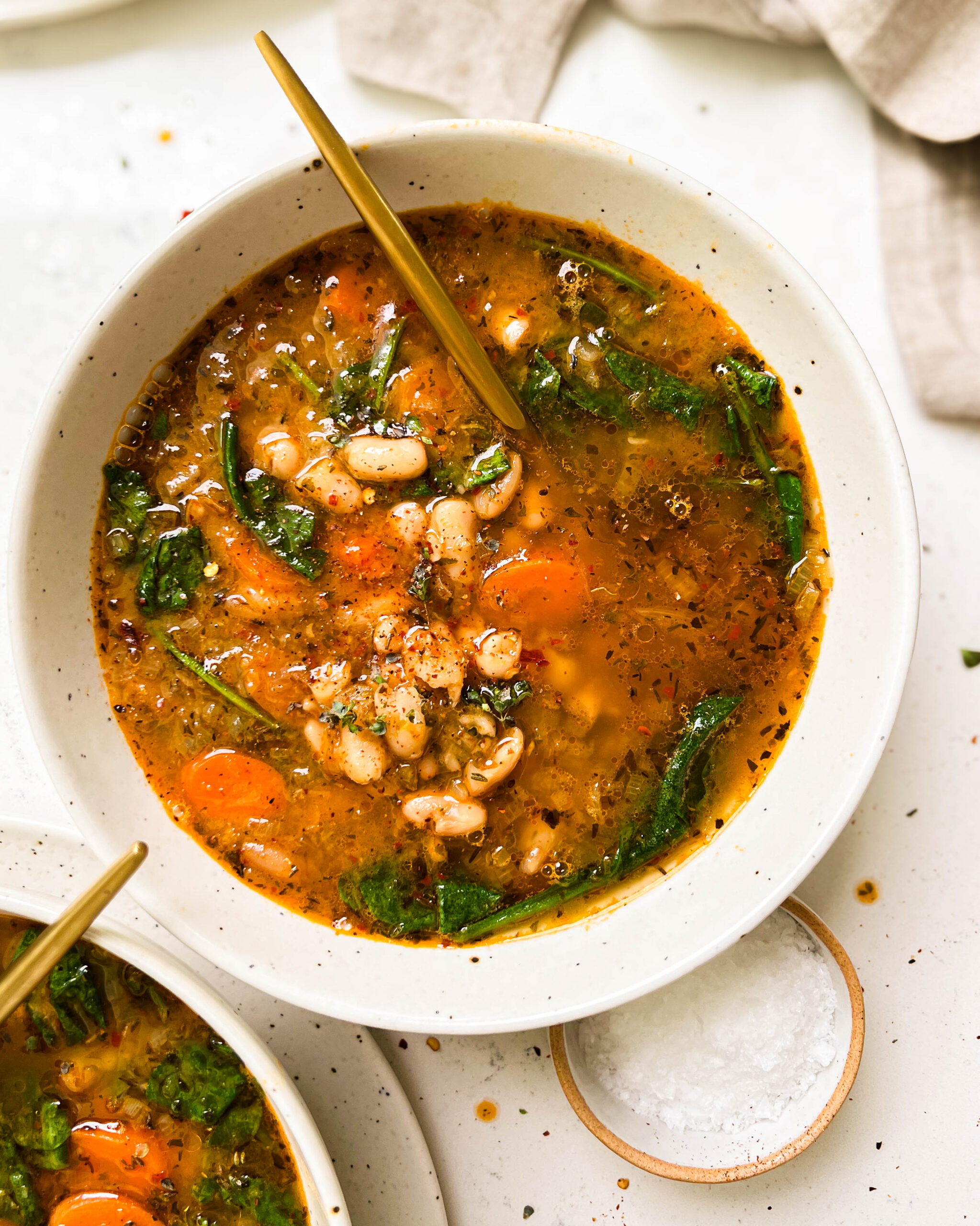 two bowls of tuscan white bean soup next to a bowl of salt and a linen cloth