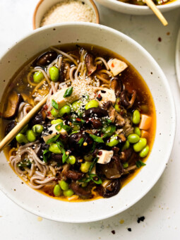 bowl of spicy mushroom noodle soup next to a bowl of sesame seeds