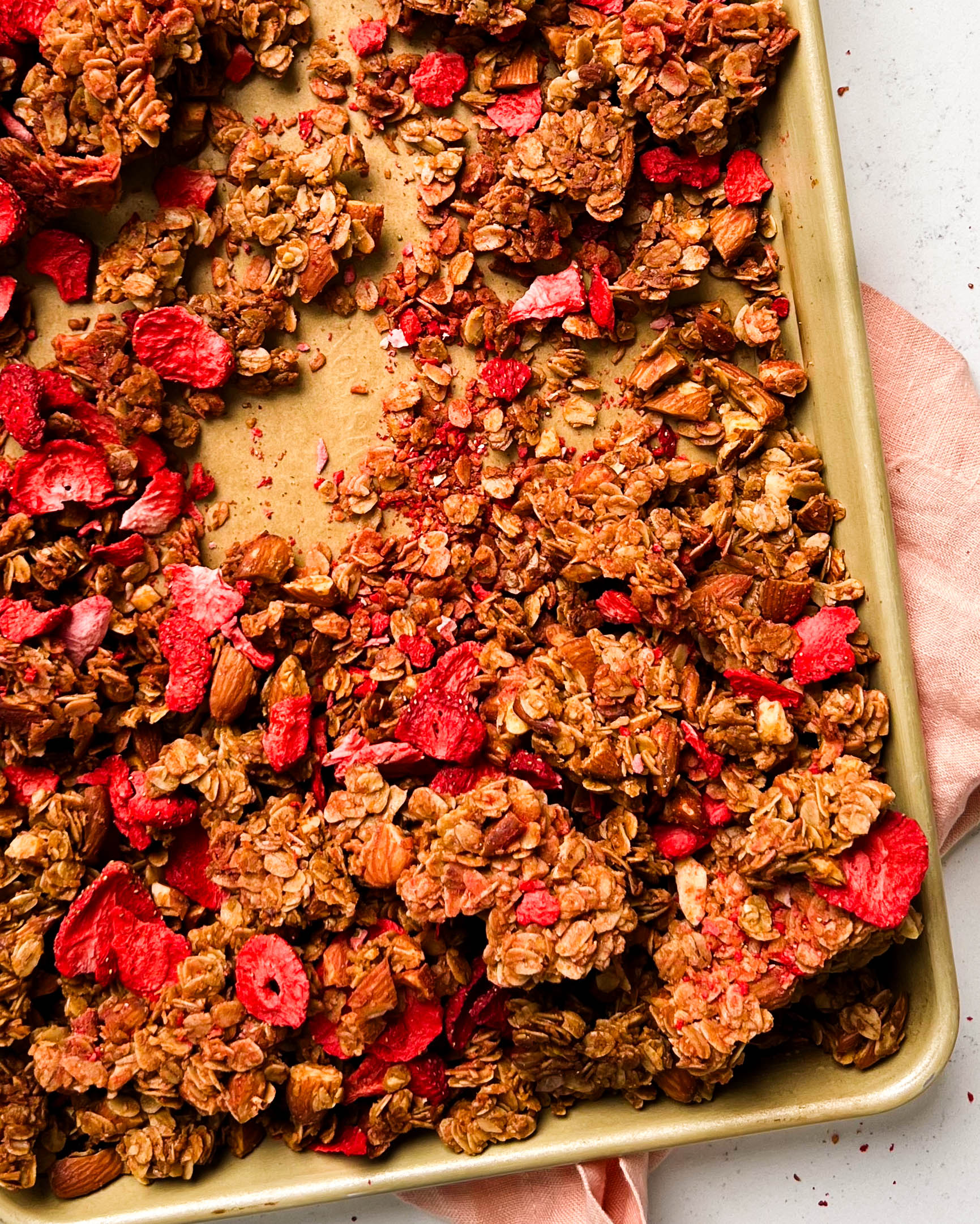 strawberry almond granola on a gold sheet pan