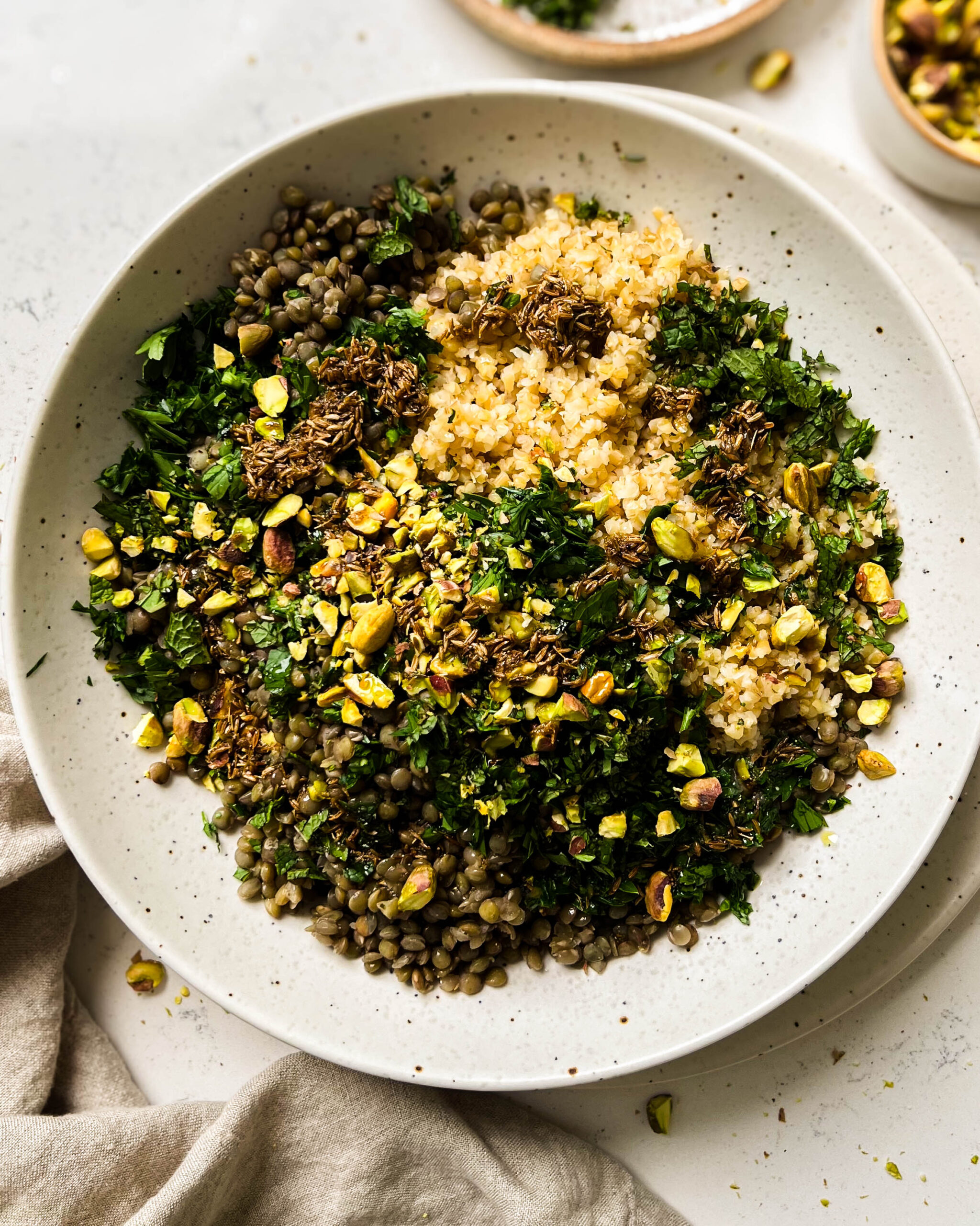 bulgur salad in a bowl next to a linen cloth and a bowl of pistachioes