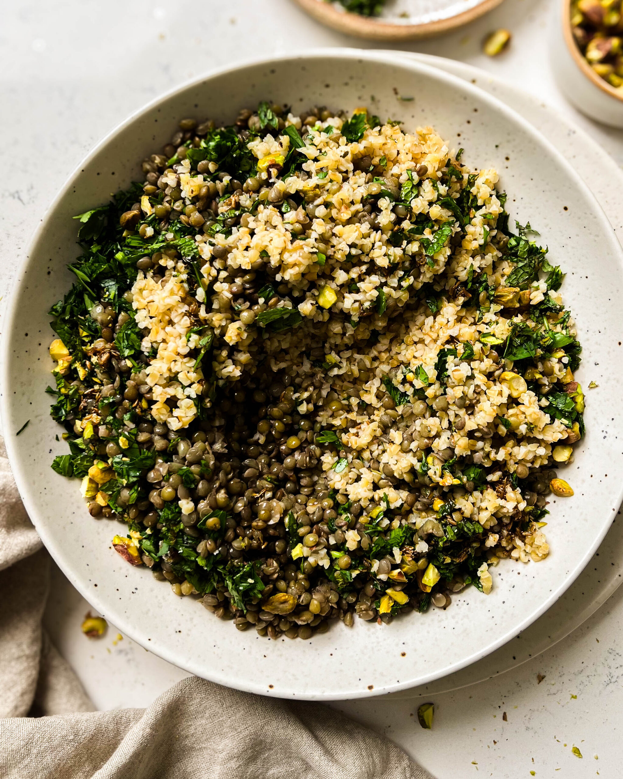 bulgur salad in a bowl next to a linen cloth and a bowl of pistachioes