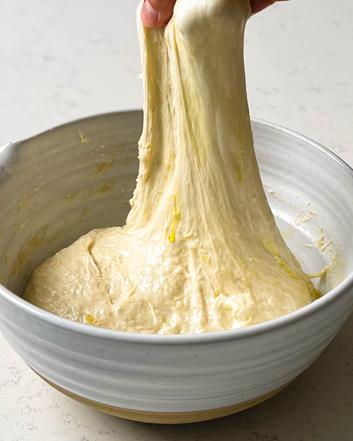 streching focaccia dough in a ceramic bowl