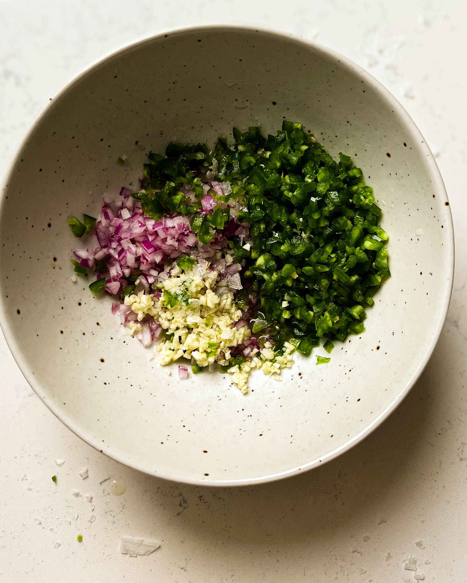 diced red onion, jalapeno, and garlic in a white speckled bowl