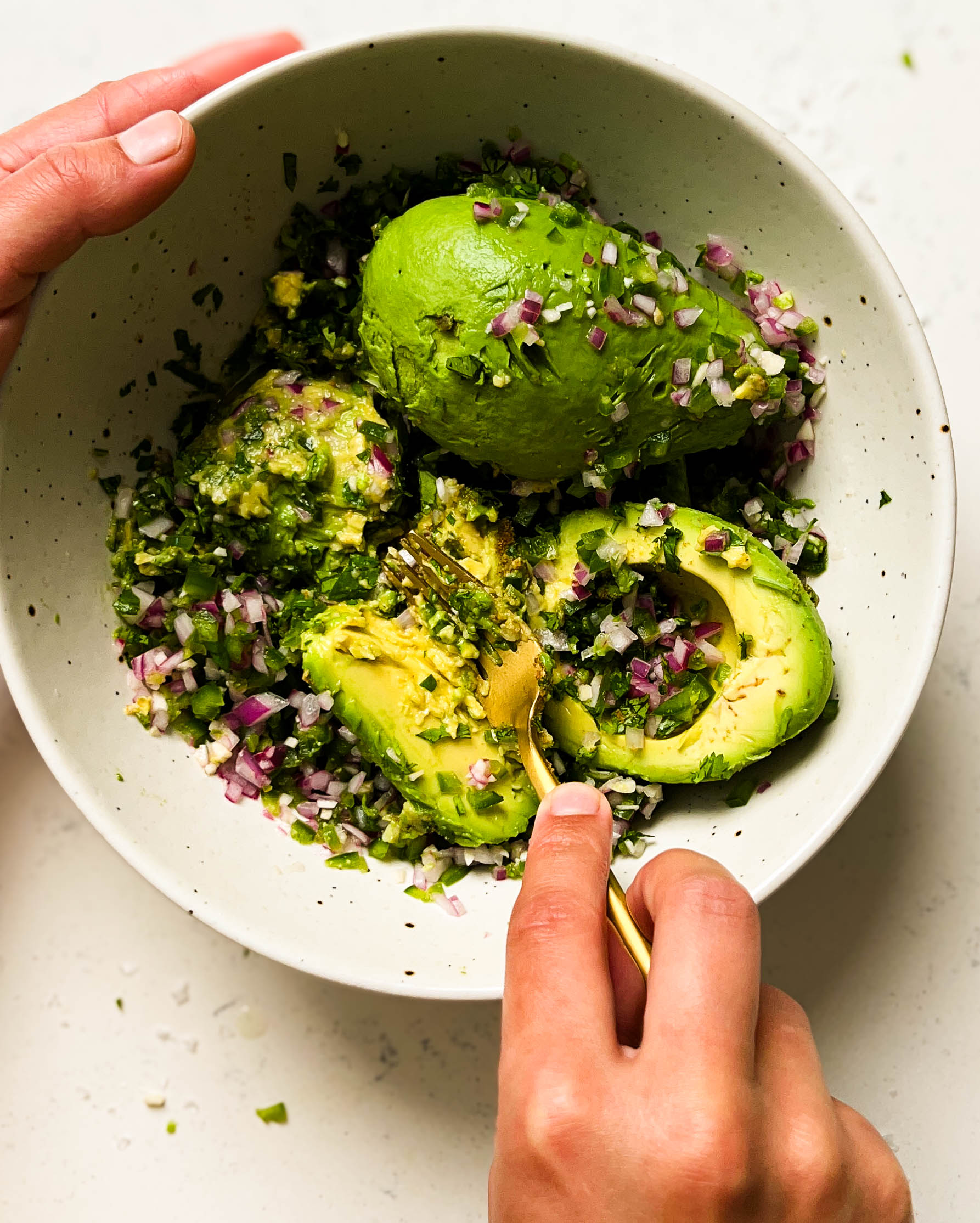 mashing avocados in a white speckled bowl