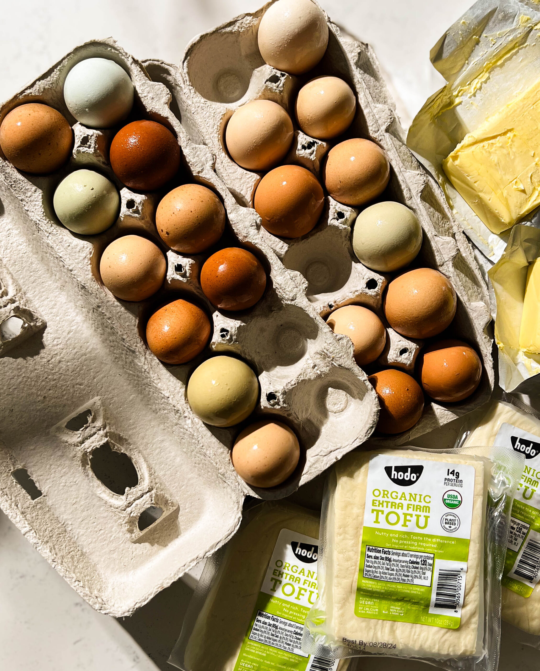 fresh eggs, tofu, and butter on a white counter