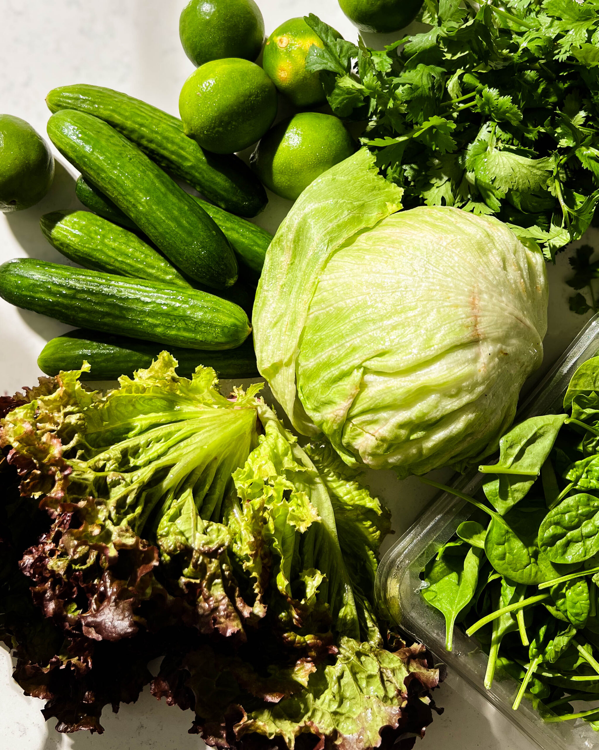 resh lettuce cucumbers,, herbs, and limes on a white counter