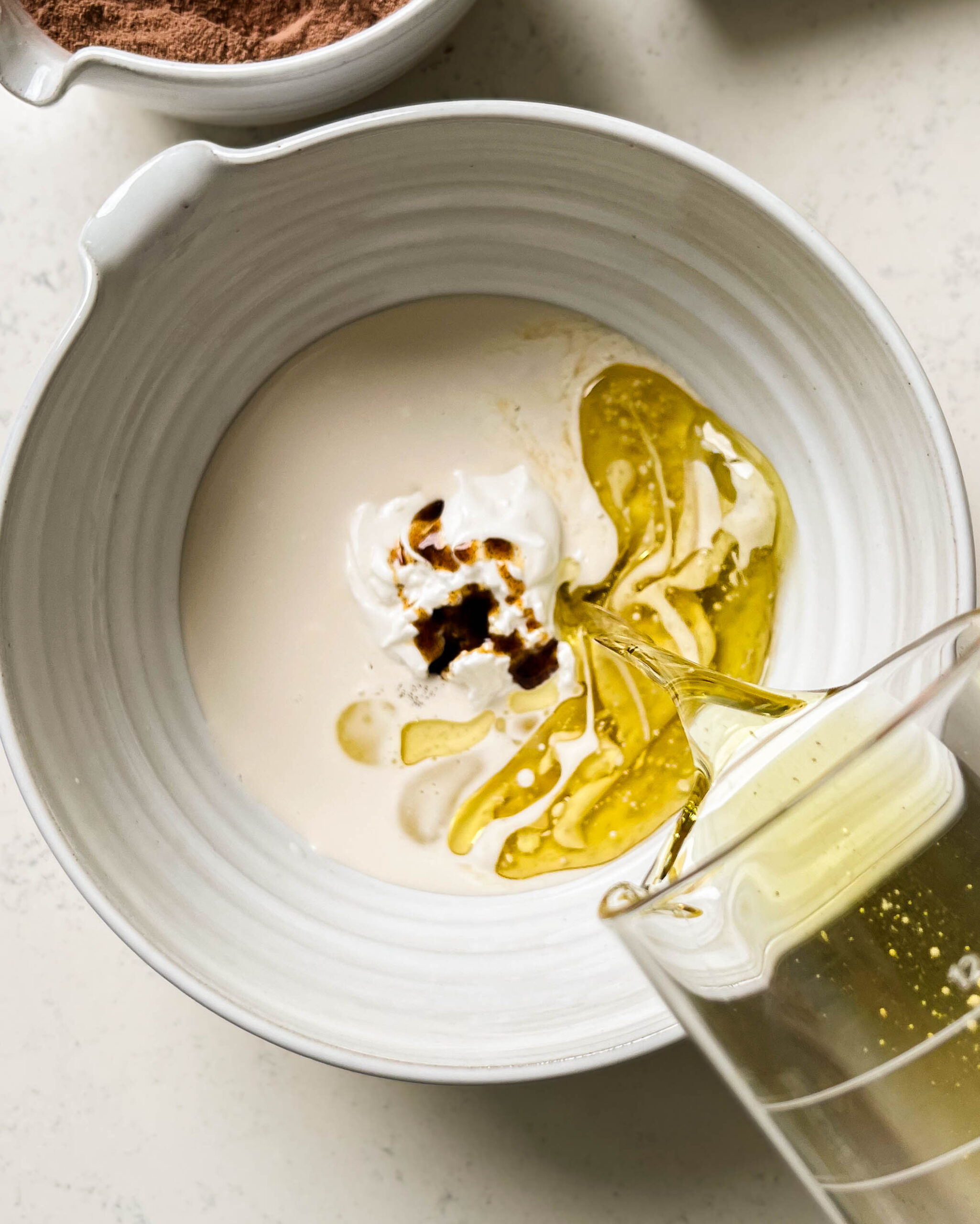 oil pouring into a big white bowl with milk and yogurt