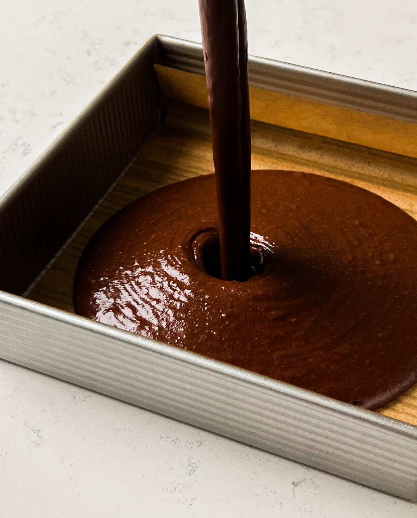 chocolate cake batter pouring into a square cake pan