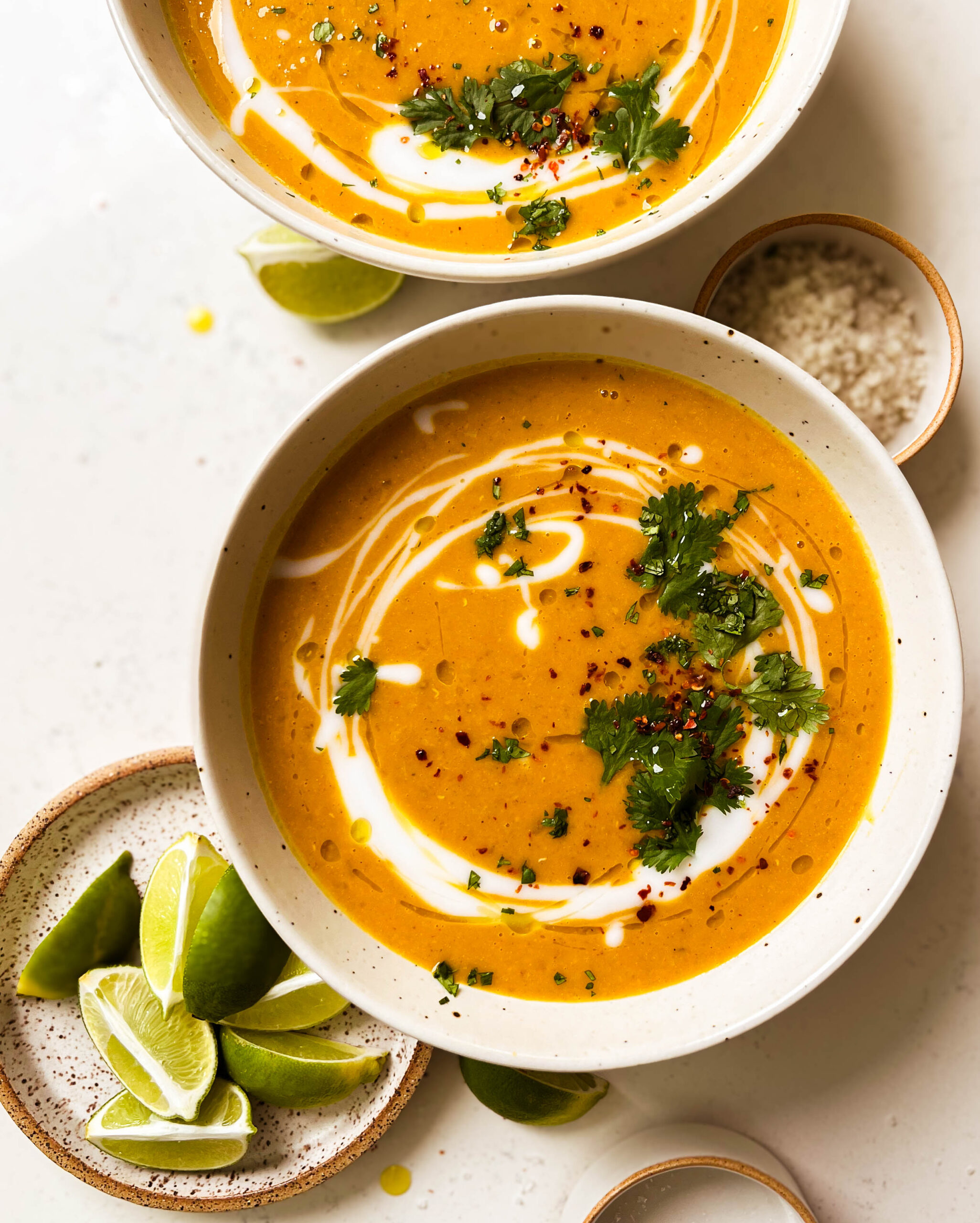 two bowls of pumpkin red lentil soup next to a plate of lime wedges