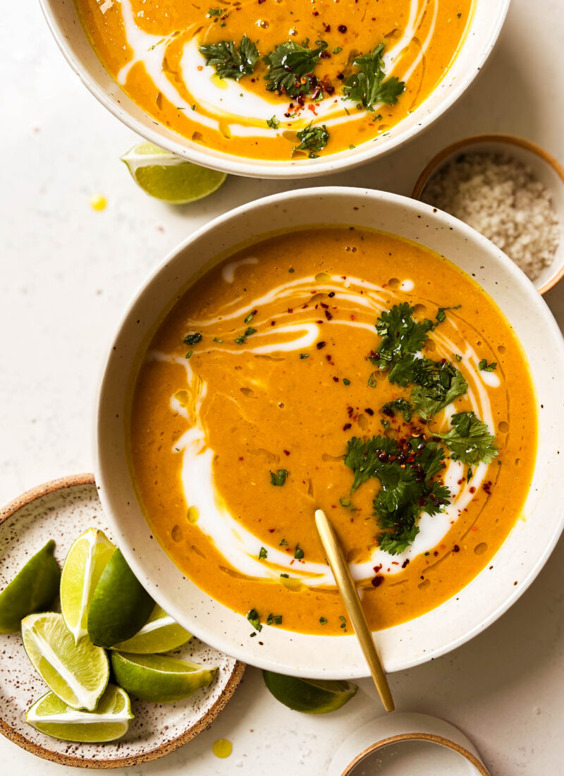 two bowls of pumpkin red lentil soup next to a plate of lime wedges