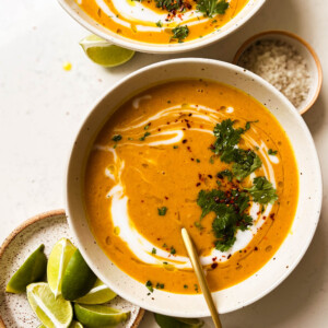 two bowls of pumpkin red lentil soup next to a plate of lime wedges