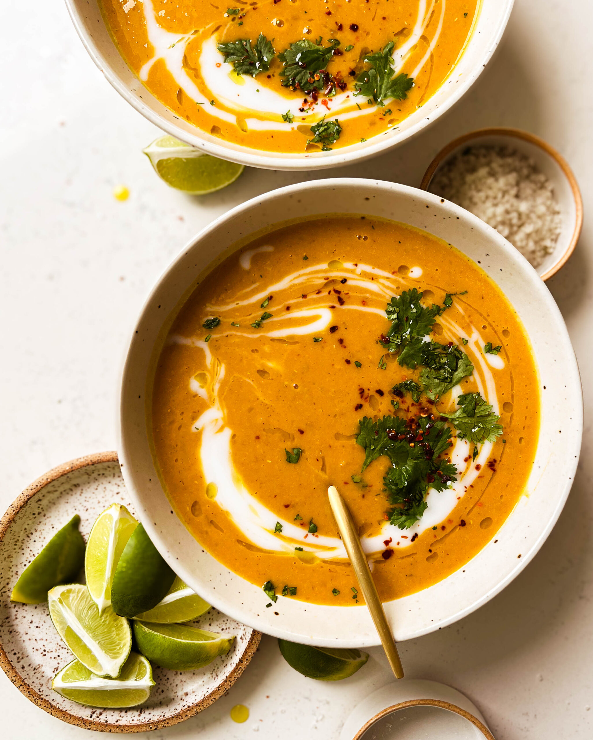 two bowls of pumpkin red lentil soup next to a plate of lime wedges