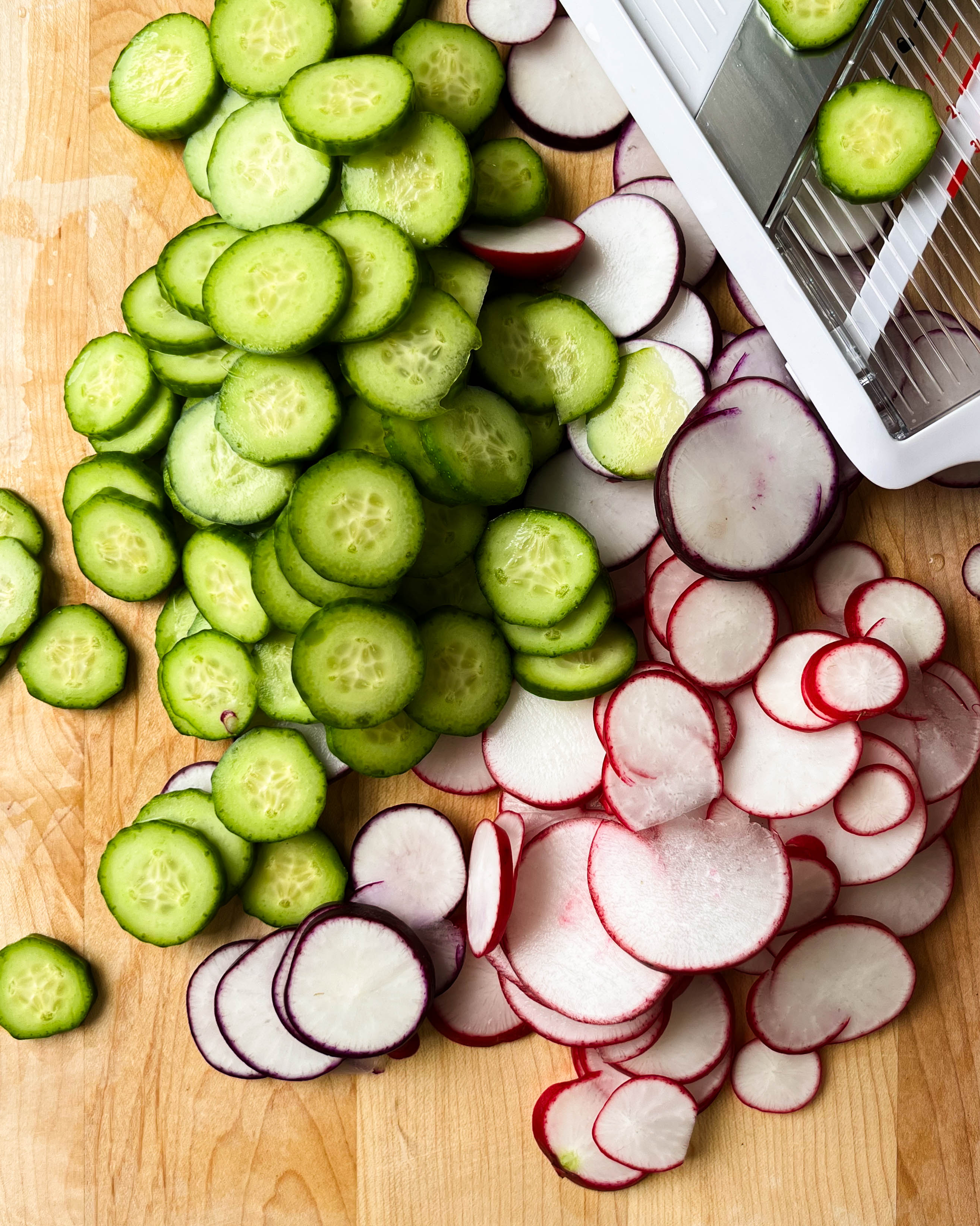 thinly sliced radishes and cucumber on a wooden cutting board